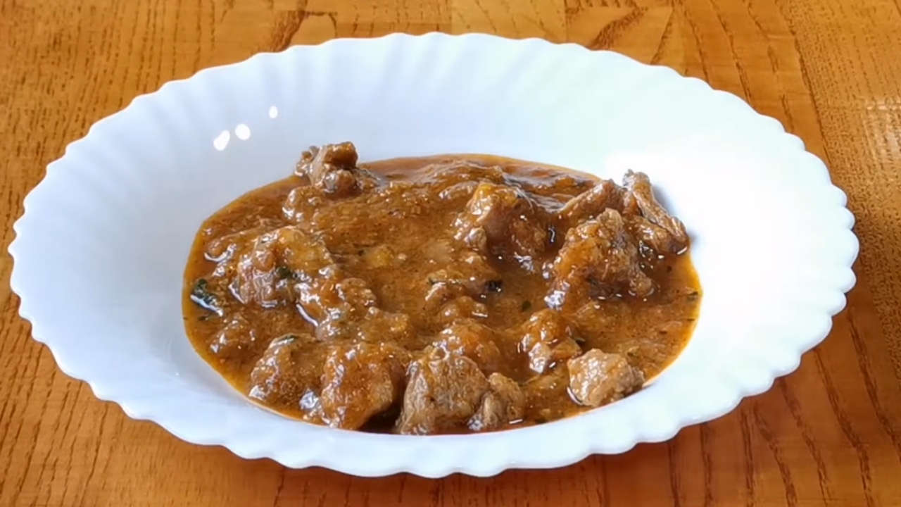 Tradicionalni mesni gulaš poslužen u belom tanjiru na drvenom stolu